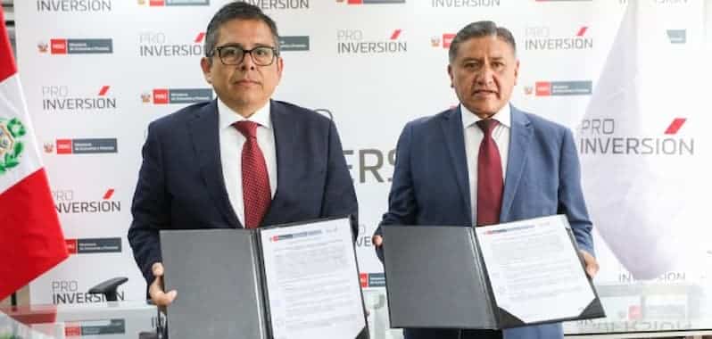 Dos funcionarios con trajes formales sostienen carpetas abiertas que contienen documentos firmados, en un evento oficial de ProInversión.