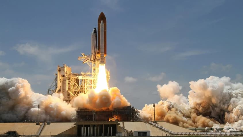 La imagen muestra el lanzamiento de un transbordador espacial desde una plataforma de despegue.