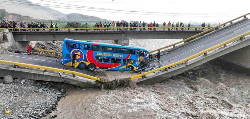 Un puente colapsado sobre un río caudaloso, con un bus de dos pisos de la empresa Cruz del Norte atrapado en la sección derrumbada. La estructura del puente se ha partido en dos, dejando al vehículo inclinado y parcialmente destruido.