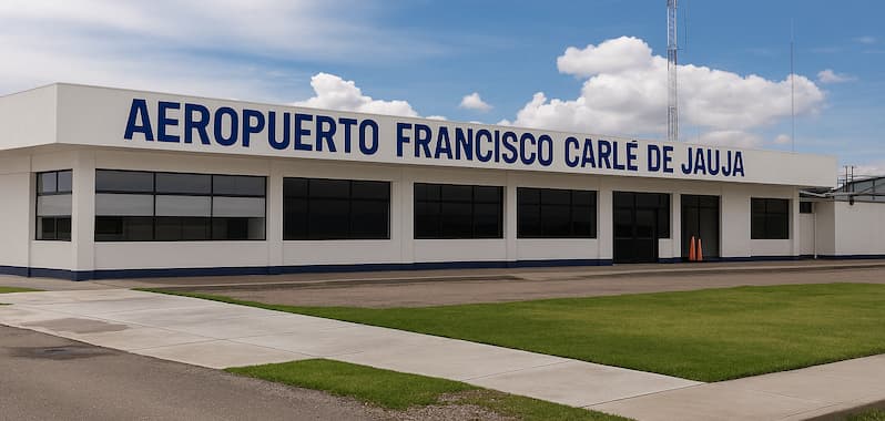 Fachada principal del Aeropuerto Francisco Carlé de Jauja, con letras azules sobre fondo blanco. El edificio presenta un diseño moderno y sencillo, con amplias ventanas y una torre de comunicaciones al fondo, rodeado de áreas verdes bien cuidadas y pavimento peatonal.