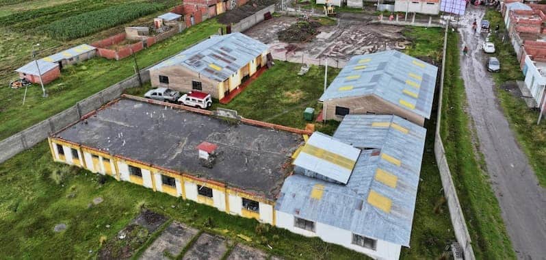 Vista aérea del Centro de Salud Yanapata, un conjunto de edificaciones de techos metálicos en un entorno rural con áreas verdes. Las estructuras presentan signos de deterioro y se ubican junto a una vía sin pavimentar, rodeadas por un muro perimetral y viviendas dispersas.