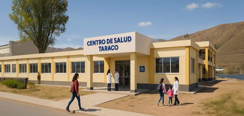 Fachada del Centro de Salud Taraco, ubicado en Puno, Perú. El moderno edificio de un nivel presenta un diseño en tonos crema y amarillo, con señalización de accesibilidad. Se observan médicos, madres con niños y usuarios ingresando al establecimiento en un entorno rural con colinas al fondo.