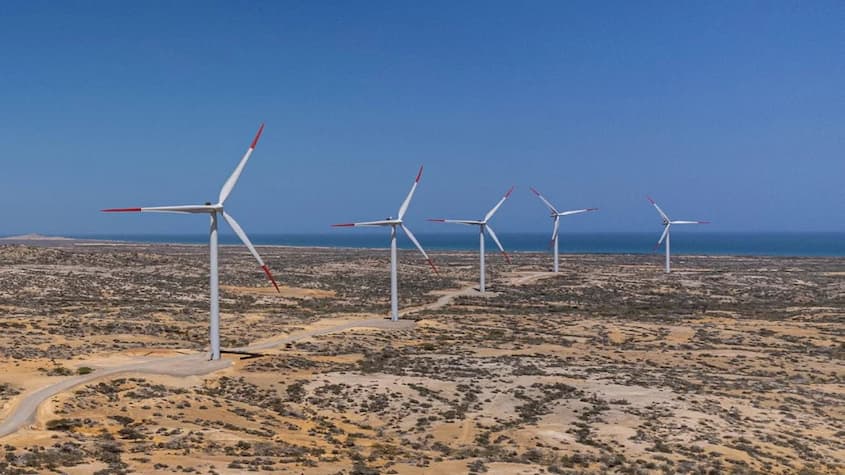 Vista aérea de un parque eólico en la costa norte de Colombia, con cinco aerogeneradores distribuidos en un paisaje árido cerca del mar. Los molinos de viento forman parte de una iniciativa de energía renovable en una zona estratégica impulsada por ECOPETROL.