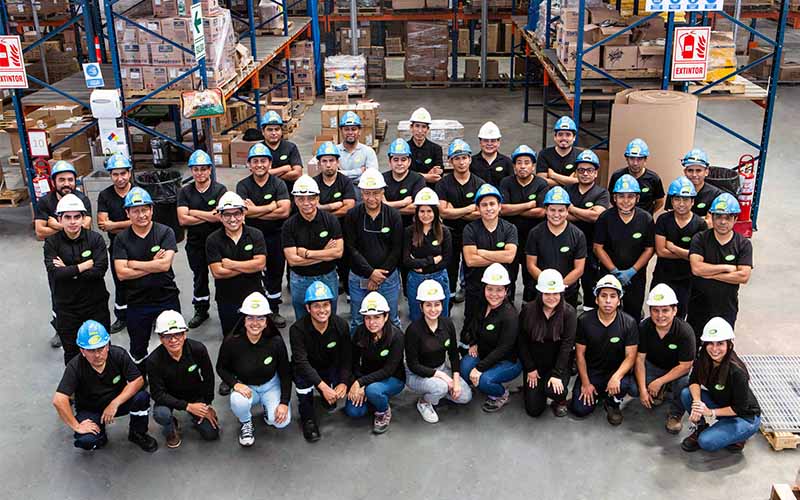 Equipo de trabajo en almacén industrial en Chorrillos, Perú, con cascos de seguridad y uniforme negro, posando para fotografía corporativa