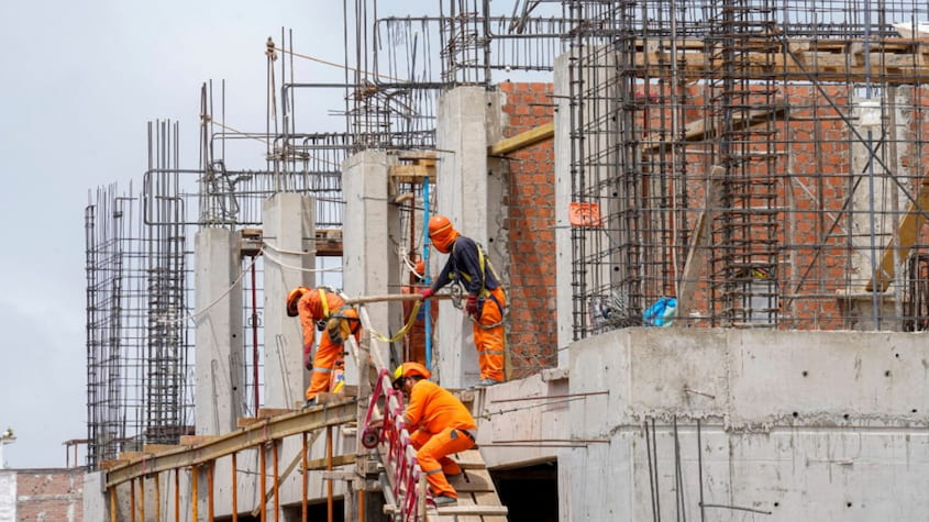 Obreros trabajando en obra de construcción con estructuras de concreto y acero en el Perú.