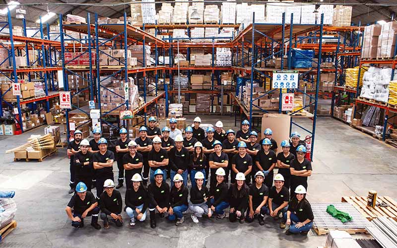 Equipo de trabajo de Efc, con cascos de seguridad posando dentro de un almacén industrial con estanterías y productos organizados, representando unidad, seguridad y compromiso laboral.