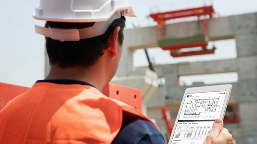 Ingeniero con casco y tablet analiza planos digitales en obra civil, aplicando inteligencia artificial para optimizar procesos constructivos.