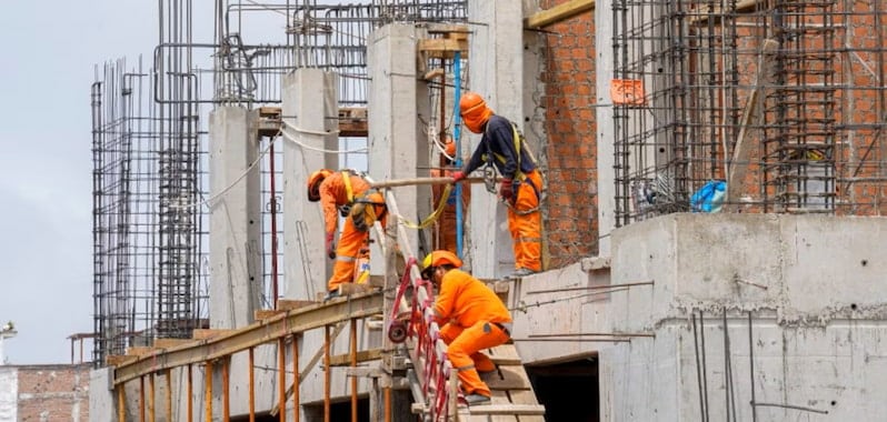 Obreros con arnés trabajan en estructura de concreto y acero en obra de vivienda, reflejo del avance del sector construcción