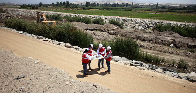Especialistas revisan planos en vía rural junto a defensas ribereñas en obras que protegen el río y la infraestructura local.